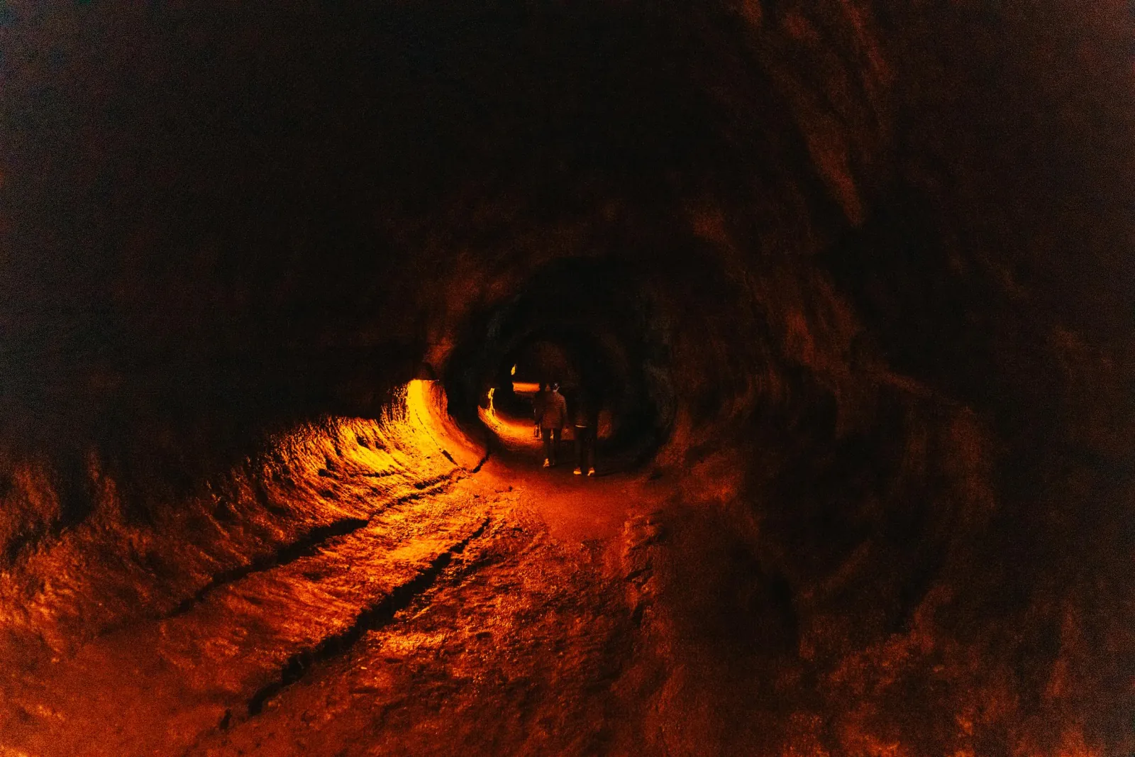 Two people walking through a dim lava tube lit in orange