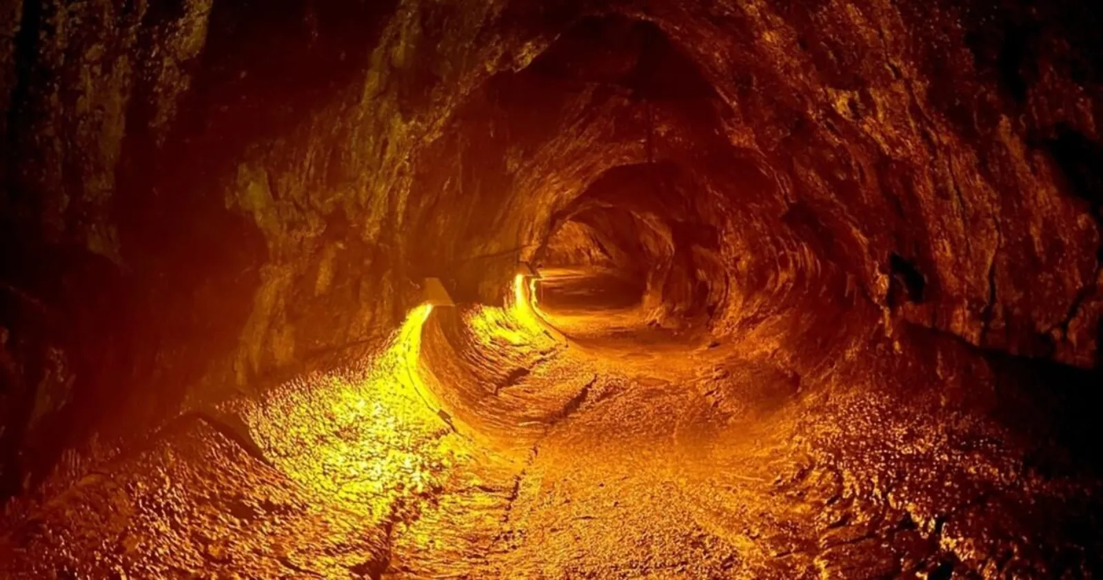 Lit lava tube with smooth rock walls and a footpath disappearing into the tunnel