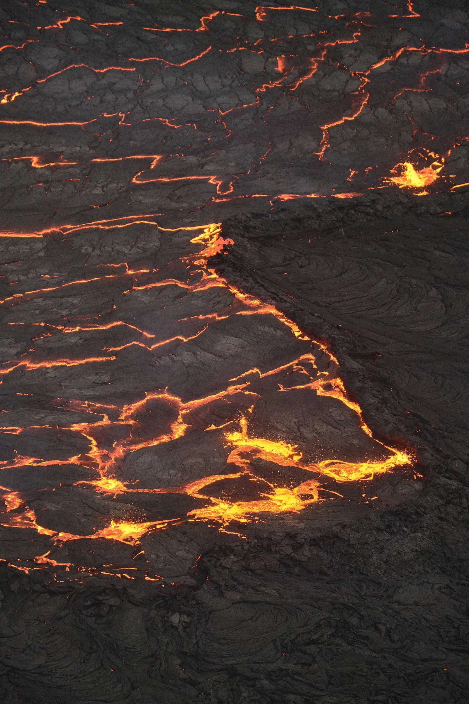 Cracked crust of a lava lake with glowing orange seams, seen from above