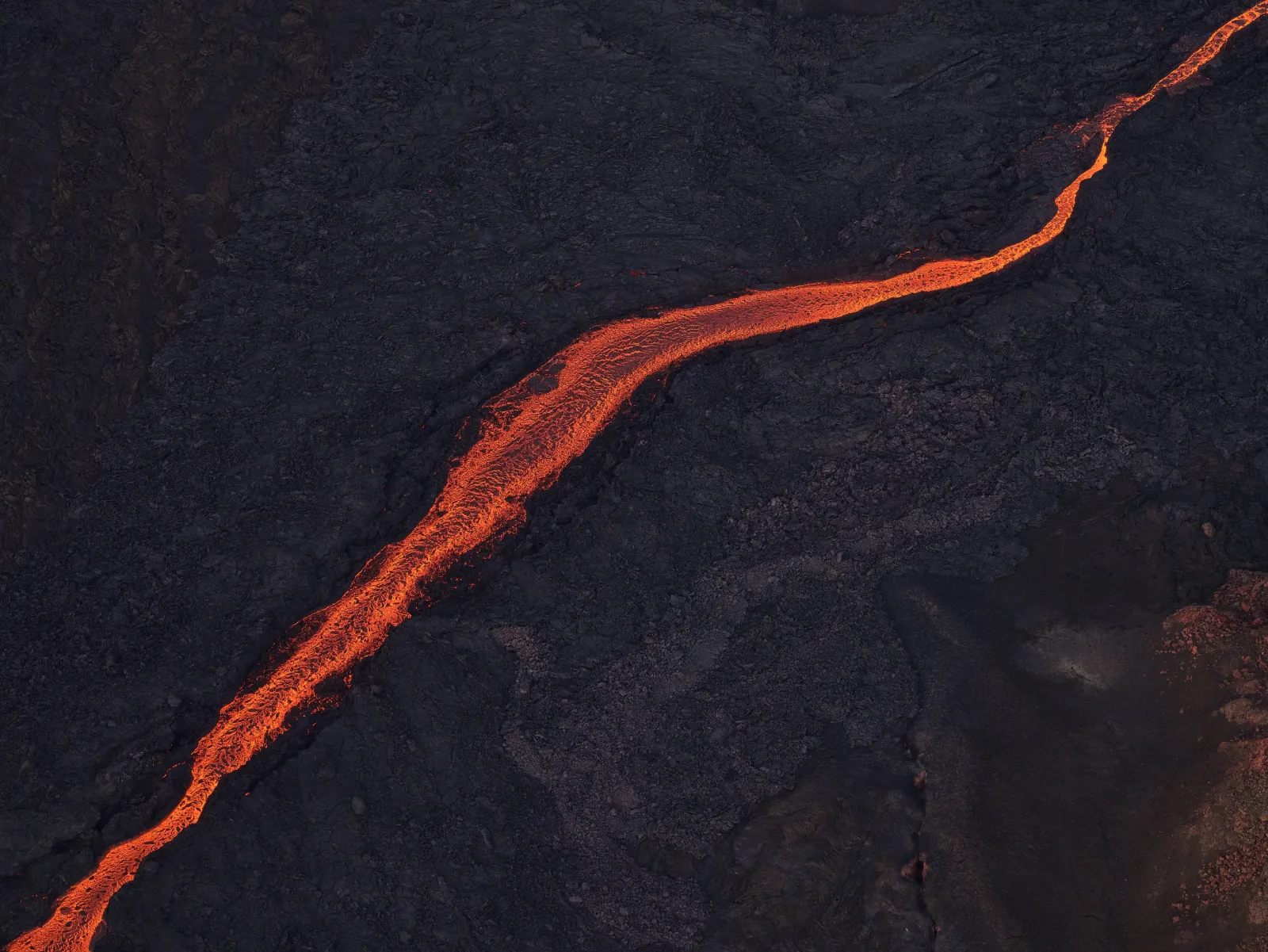 A single glowing lava channel winding across black lava, seen from above