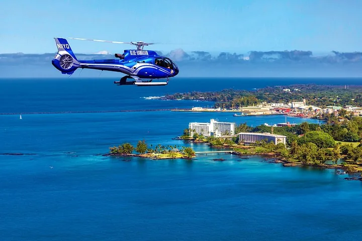 Blue Hawaiian helicopter over a sunny bay with hotels, a small palm islet and town