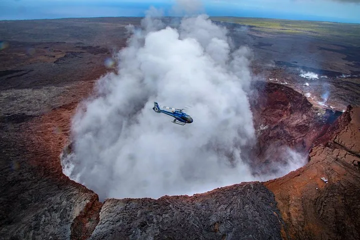 Helicopter hovering over a steaming volcanic crater surrounded by dark lava fields