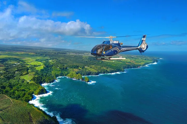 Helicopter cruising above a lush green coast where white surf meets deep blue water
