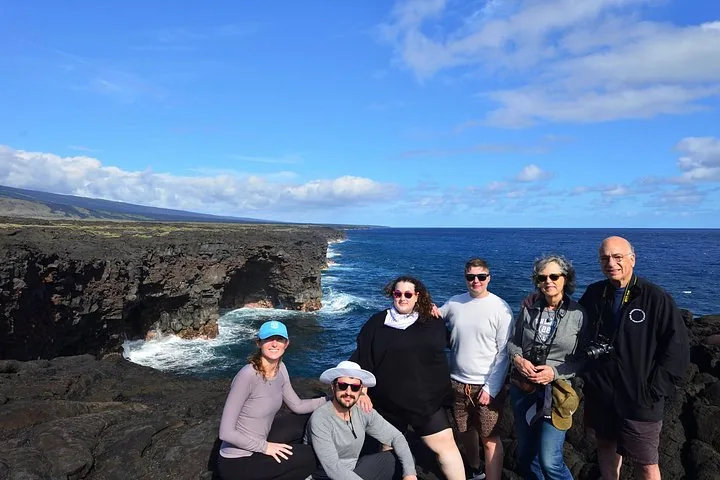 Tour group posing on black lava sea cliffs above crashing surf on a sunny day