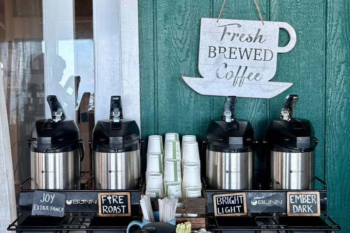 Fresh Brewed Coffee sign above four coffee dispensers and stacked paper cups