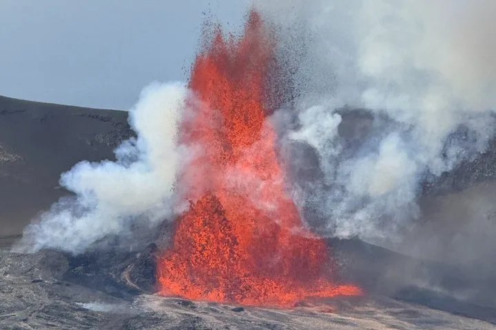 Orange lava fountain bursting from a vent amid white steam and dark cinder slopes