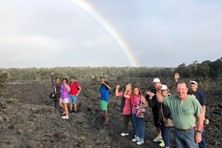 Group waving on a rough lava field with a rainbow arcing over the forest