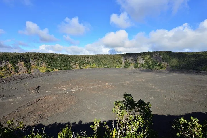 Wide crater floor of solidified gray lava ringed by forested cliff walls
