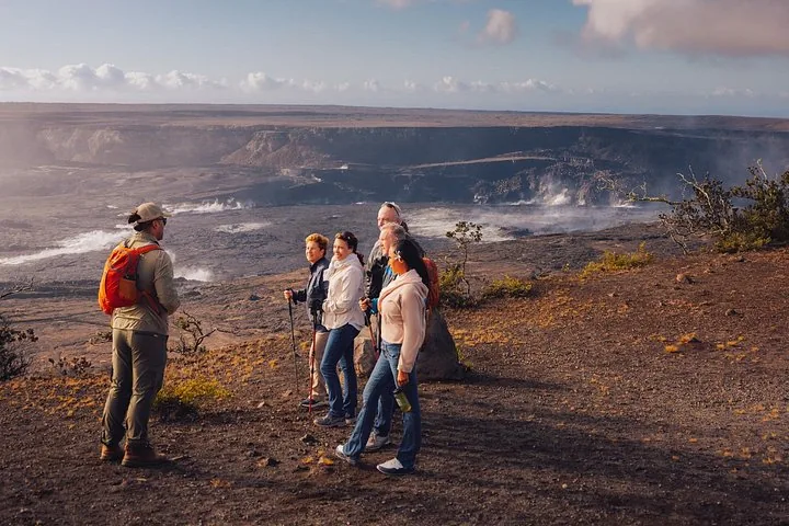 Guide with an orange daypack talking to guests at an overlook above the steaming Kīlauea caldera