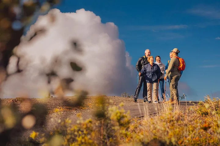 Guide and smiling guests with trekking poles on a path beside a billowing steam cloud