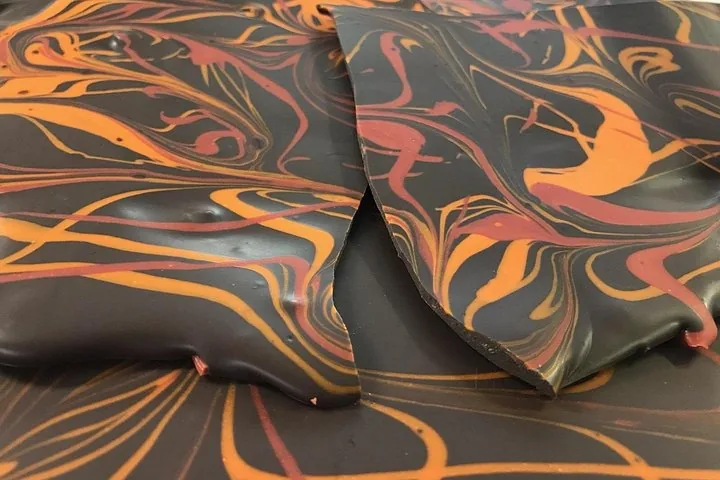 Close-up of broken dark chocolate bark swirled with orange and red patterns