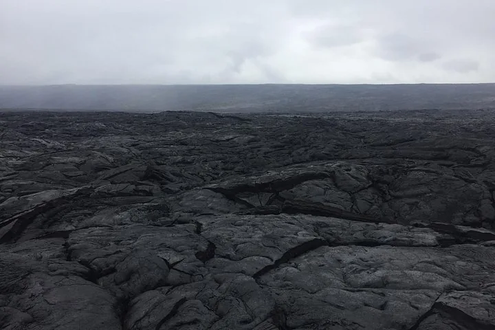 Wide field of cracked black lava stretching to the horizon under a misty sky