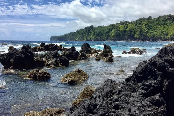 Black lava rocks and tide pools along a green cliff-lined coast