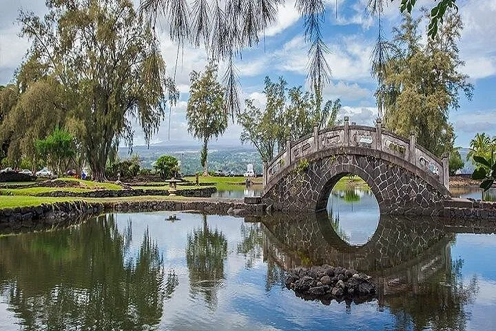 Arched stone footbridge reflected in a calm pond in a landscaped park