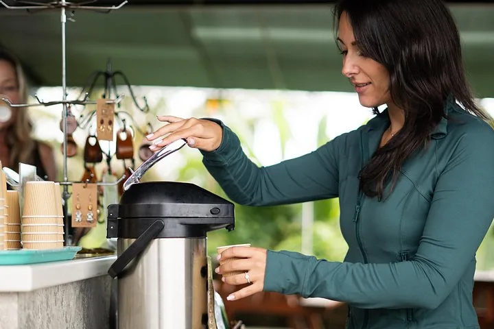 Guest filling a paper cup from a coffee dispenser at a farm tasting bar