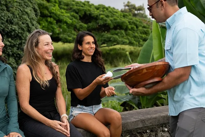 Guide serving pastries from a wooden bowl to smiling guests seated on a stone wall
