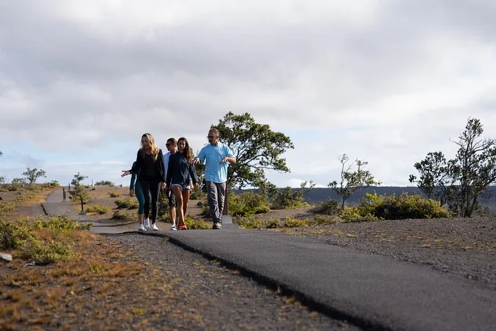 Small group walking a paved path through dry scrubland under a cloudy sky