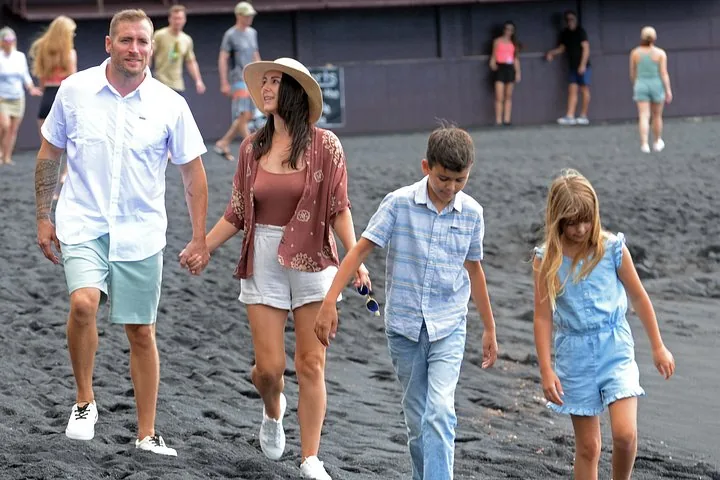 Family of four walking across a black sand beach with other visitors behind them