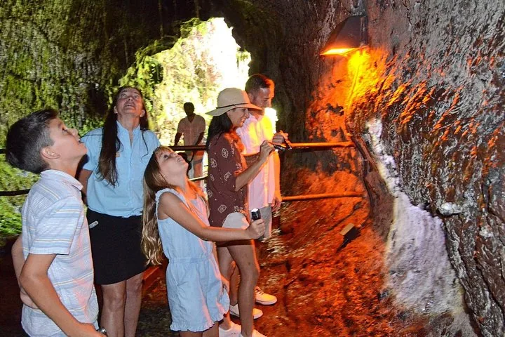 Family looking up at the orange-lit rock walls inside a lava tube