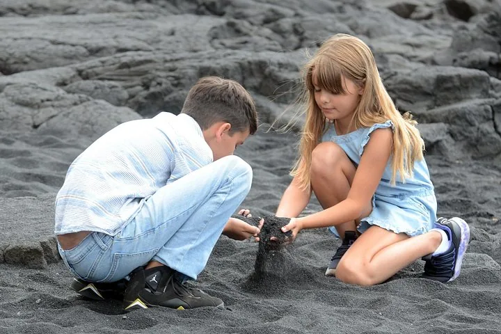 Two children letting black sand run through their hands on a lava shore
