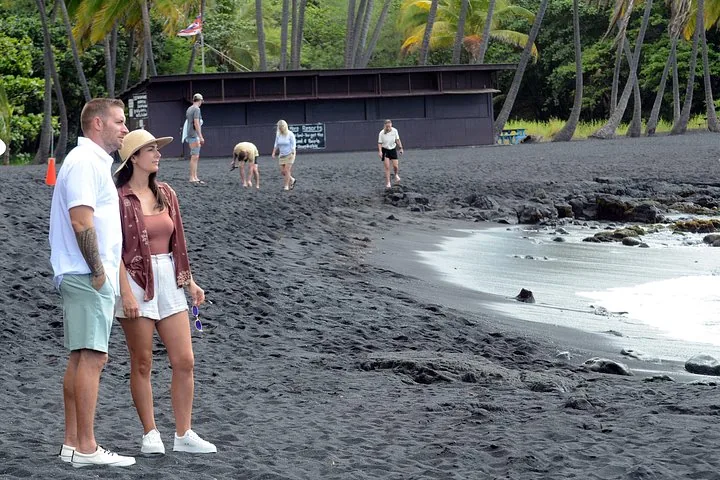 Couple standing on a black sand beach by the surf with palm trees behind